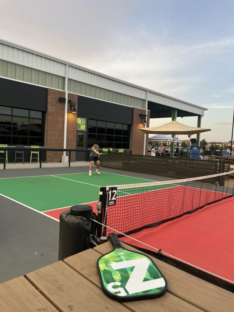 Man playing pickleball on an outdoor Chicken N Pickle court with an ONIX paddle in the foreground.