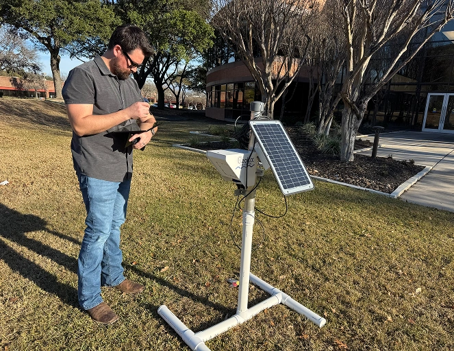 Engineer recording data on a tablet next to a solar-powered monitoring station