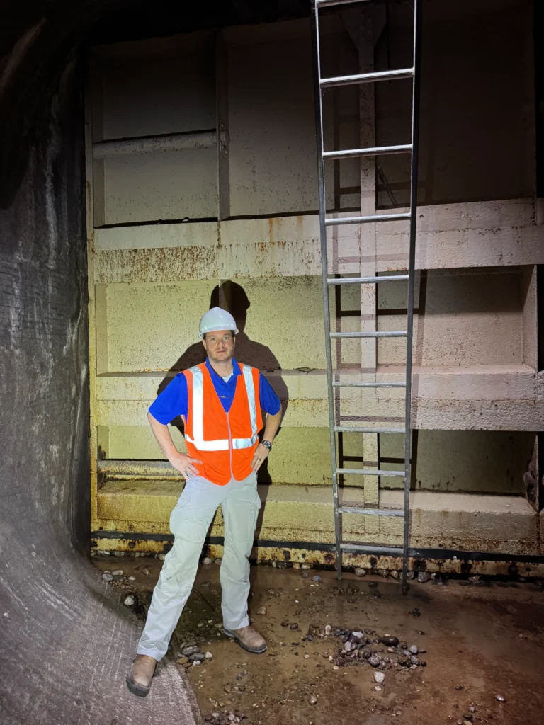 Engineer in a hard hat and safety vest inspects a large flood-control gate inside a drainage tunnel.