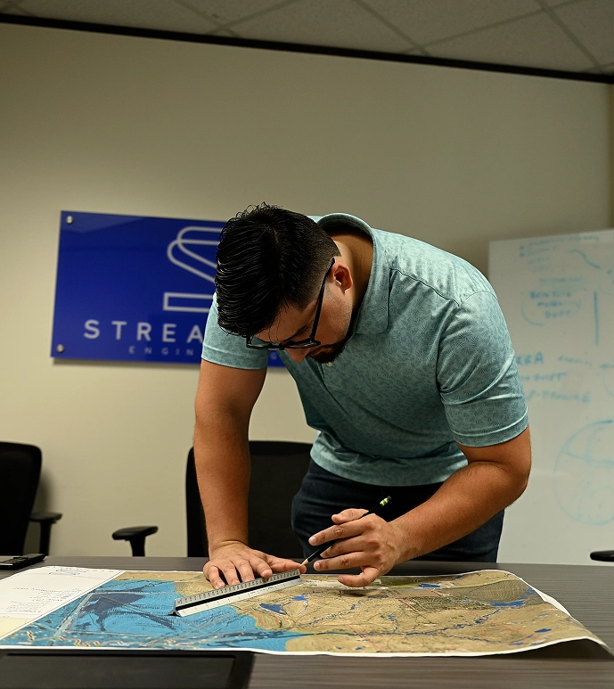 Engineer measuring a floodplain map with a scale ruler in the Streamline Engineering office