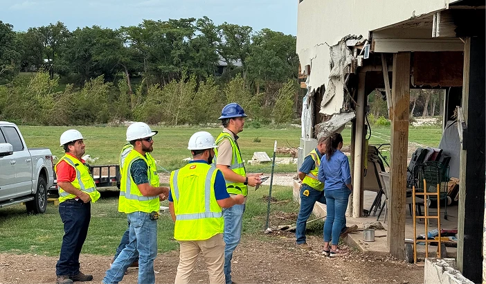 Engineers in hard hats and safety vests assessing a storm-damaged building