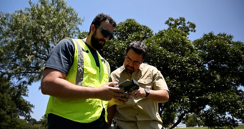 Two field engineers reviewing a drone controller during an outdoor site survey.